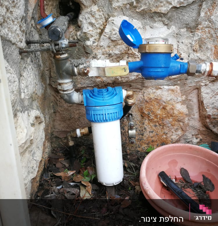 מד מים כחול עם צינורות וברזים על קיר אבן